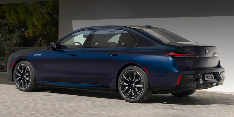 A silver BMW iX electric SUV charging at a modern green-accented charging station outdoors